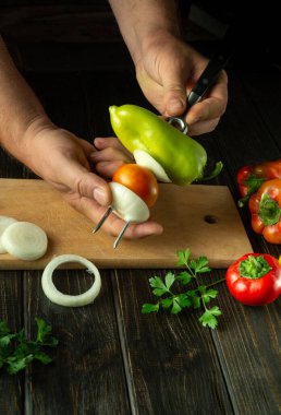 Piknik için taze sebze hazırlıyorum. Bir adam mutfak masasının üzerinde çatalla biber şişini uzatıyor. Siyah panodaki reklam alanı.