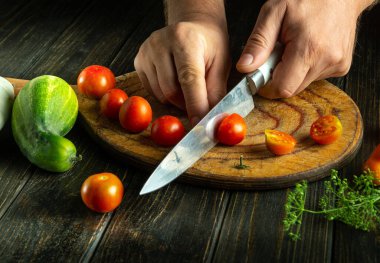 Şef kahvaltı hazırlığı için mutfak masasında kiraz domatesini bıçakla keser. Sebze karışımı pişirme konsepti.