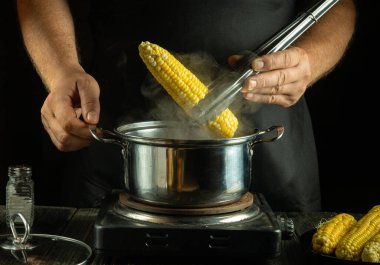 Restoran mutfağında haşlanmış mısır pişirmek. Aşçı, elinde maşayla bir mısır kamışı patlattı..