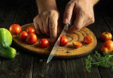 Domatesle yemek pişirmek. Erkek ellerinin evdeki mutfak tahtasına bıçakla kiraz domateslerini kestiği yakın plan..