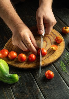 Kiraz domatesli sağlıklı bir kahvaltı. Aşçı mutfak masasında sebze salatası hazırlar. Şefin elinde bıçakla domates doğramak..