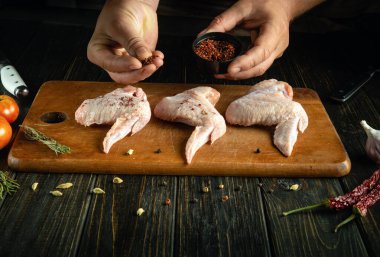 Cooking chicken wings with spices for flavor and aroma. Close-up of a cook hand adding dry spices to raw chicken wing. clipart