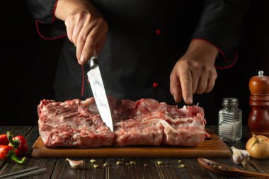 Bir şef büyük bir parça eti kesme tahtasındaki bir bıçakla kesmeye çalışır. Baharatlı mutfak masasında çiğ biftek kaburgası..