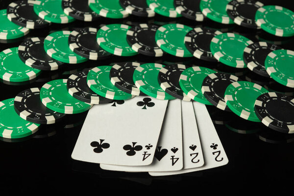Playing cards with a combination of two pairs and chips in the background received from winning. Concept of winning in a casino on a black table.