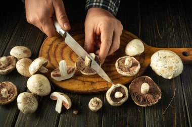 Şef lezzetli yemekler hazırlamak için Agaricus mantarını bıçakla keser. Antika mutfak masasında şampiyon mantarları. Kahvaltı veya öğle yemeği için lezzetli bir tarif..
