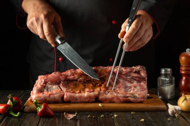 Şef çiğ et hazırlıyor. Kızarmadan önce büyük bir parça pirzola hazırlıyorum. Et kesmeden önce mutfak masasındaki kasapın elindeki çatal ve bıçak..