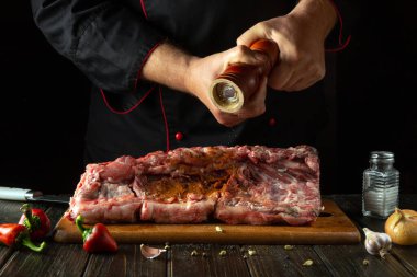 Adding pepper to raw meat manually by a chef for aroma and flavor. The process of cooking beef ribs on the kitchen table with spices and pepper. clipart