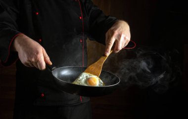 Bir şef, akşam çöktüğünde sıcak mutfağı dolduran dalgalı buharla çevrili, mükemmel pişmiş, güneşli bir tavada yumurtayı ustaca çevirir..