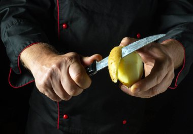 Odaklanmış elleri olan yetenekli bir şef, keskin bir bıçakla karanlık bir mutfak zeminine karşı patates soyar. Atmosfer mutfak hazırlıklarının sanatsallığını vurguluyor..