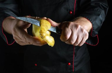 Siyah üniformalı bir şef patatesi ustalıkla soymak için keskin bir bıçak kullanır. Odaklanma aktivitesi loş aydınlatılmış bir mutfakta geçiyor..