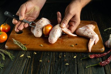 Eller titizlikle tavuk kanatları ve olgun domatesleri tahta kesme tahtasına dizer. Aromatik otlar ve baharatlar taze malzemelerin etrafını sarar, canlı bir aşçılık deneyimini güçlendirir..