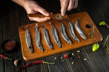 Yetenekli bir el, ahşap bir tahtanın üzerine serilmiş taze balıkları dikkatlice kokulu baharatlar serpiştirmek için tahta bir kaşık kullanır. Sıcak mutfak yemek pişirmede yaratıcılığı davet eder..