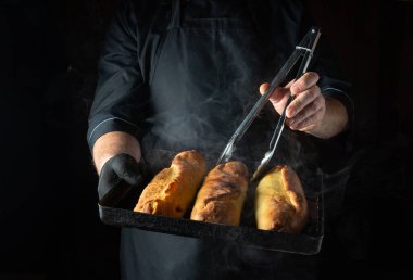 Bir şef zarifçe bir tepsi altın sarısı rulo tutar, etrafında buhar döner. Koyu arkaplan, pişmiş yiyeceklerin dokusunu ve sıcaklığını vurgulayarak, sıcak parıltıyı arttırır..