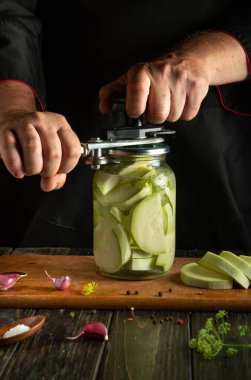 Yetenekli eller, gevrek sebzeler, mis kokulu otlar ve baharatlarla dolu bir kavanozu özenle kapatarak çalışırlar. Kırsal bir ahşap masa lezzetli bir mutfak geleneği için gerekli malzemeleri barındırır..