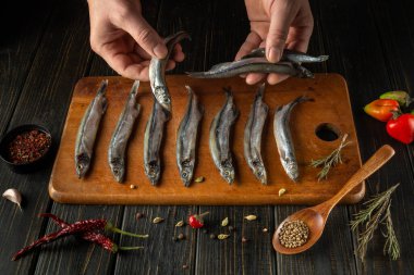 Eller, yakınlarda bitkiler, baharatlar ve renkli biberlerle ahşap bir kesim tahtasına dikkatlice taze balık yerleştirir..