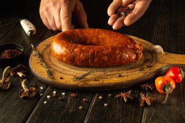 Uzman eller, ahşap bir tahtanın üzerinde duran büyük, el yapımı bir sosisi geliştirmek için aromatik baharatlar seçerler. Taze biber ve otlar yemek sanatının yaratıcılığını ön plana çıkarıyor..