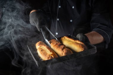 Sıcak buhar, aşçıyı yeni pişmiş ekmeklerle dolu bir tepsiyi tutarken sarar. Narin altın hamuru parıldıyor, davetkar bir zevk veriyor..