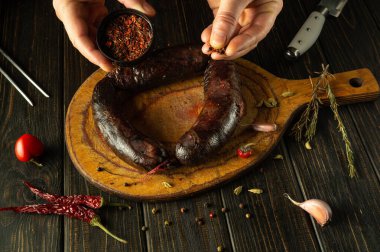 Yetenekli bir şef, ahşap kesme tahtasına bir dizi baharat koyarak nefis bir sosis hazırlar. Aşçılık sanatına ve taze malzemelere olan sevgisini gözler önüne serer..