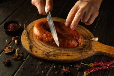 Sıcacık aydınlatılmış bir mutfakta, becerikli eller, rustik ahşap bir tahtanın üzerinde duran zengin, aromatik bir sosisi dilimler. Bitkiler ve baharatlar mutfak sanatını geliştirmek için sahnenin etrafını sarmış..