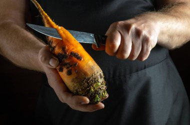 Odaklanmış eller parlak turuncu bir havucu kavrayıp ustalıkla deriyi keskin bir bıçakla yüzüyor. Kırsal mutfak atmosferi, yaratıcılık sürecine taze malzemeler hazırlama sıcaklığını katıyor..