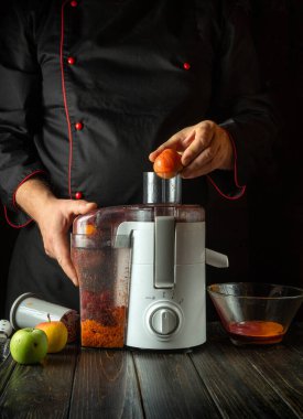 Bir şef, elektrik sıkacağının içine elle çiğ elma ekler. Akşam yemeği için otel mutfak masasında sağlıklı meyve suyu hazırlıyorum..