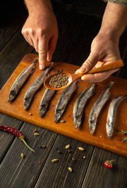 Yetenekli eller, ahşap bir tahtaya taze balık yerleştirir, küçük bir kaşıktan baharat eklerken canlı biberler ve bitkiler mutfak atmosferini geliştirir..