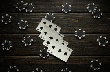 Siyah poker çipleriyle çevrili ahşap bir yüzey üzerinde maça ve haçlarla oynanan iskambil kağıtları var. Oyuncular oyuna dahil olurken atmosfer beklenti ve stratejiyle doludur..