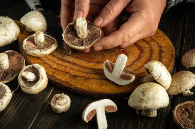 Hands are skillfully slicing and preparing fresh mushrooms on a wooden cutting board surrounded by a variety of freshly picked fungi. The warm ambiance of the kitchen enhances the experience. clipart