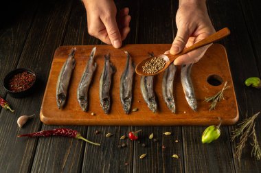 Elleri ustalıkla, kırsal kesim tahtasına taze balık serpiştirip aromatik otlar ve baharatlar serpiyor. Sıcak bir mutfak havası yemek sanatını ve lezzetli bir yemeğin beklentisini arttırır..