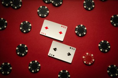 Bir çiftin kazanan kombinasyonuna sahip bir çok iskambil kağıdı bir kulüpteki kırmızı masada, çiplerle çevrili. Atmosfer beklenti ve poker stratejisiyle dolu..