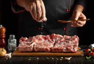 Yetenekli bir şef ahşap kesme tahtasındaki büyük bir parça çiğ etin üzerine ustalıkla tuz serper..