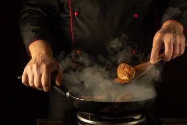 Bir şef, pişirme tekniklerini sergilemek için buharla dolu bir tavada ustalıkla altın-kahverengi köfteler çeviriyor. Koyu arkaplan, bu mutfak anının yoğunluğunu arttırıyor, sanatın altını çiziyor..