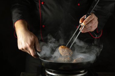 The chef, dressed in a black robe with red accents, expertly holds a fork to sear a cutlet in a frying pan. Steam rises sharply, creating an atmosphere of intense culinary focus. clipart