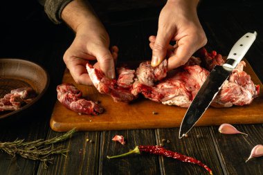 Eller, taze otlar ve canlı biberlerle çevrili ahşap bir tahtanın üzerinde ustalıkla eti kesiyor. Ortam, mutfak işçiliği ve geleneksel tekniklere olan tutkuyu yansıtıyor..