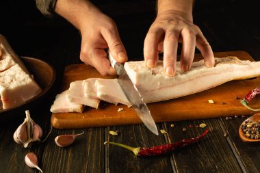 Yetenekli bir şef, ahşap kesme tahtasındaki kalın bir domuz göbeğini kesmek için keskin bir bıçak kullanır..