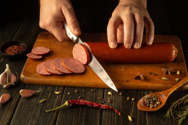 Hands skillfully cut through a rich sausage on a wooden board, surrounded by spices, garlic, and vibrant herbs. The warm atmosphere exudes culinary tradition and passion for food. clipart