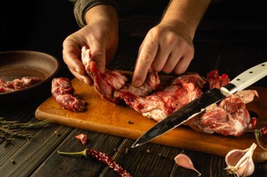 Eller ahşap bir tahtanın üzerinde çeşitli et parçalarını ustalıkla inceliyor. Yetenekli bir teknik ve aşçılık tutkusunun bir karışımını sergiliyor. Kırsal atmosfer kasaplığın sanatını güçlendiriyor..