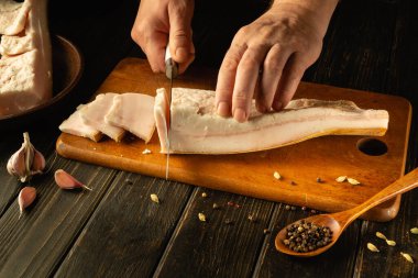 Sarımsak karanfili ve baharatlarla çevrili ahşap bir tahtanın üzerindeki taze domuz yağını ustalıkla kesiyorlar. Sıcak ışık, bu yemek pişirme anının kırsal duygusunu arttırıyor..