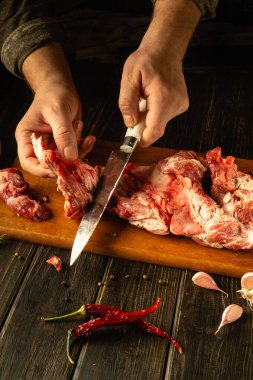 Ahşap bir tahtanın üzerinde, canlı baharatlar ve sarımsak ile çevrili çiğ kuzu etini ustalıkla kesiyorlar. Kırsal mutfağın sıcacık parıltısı doyurucu bir yemek hazırlığını güçlendirir..