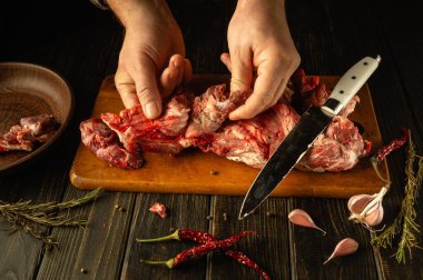 Eller, sarımsak, kurutulmuş biber ve bitkilerle çevrili ahşap bir tahtanın üzerinde ustalıkla kesilmiş ve taze et seçimi hazırlıyorlar. Sıcak atmosfer önümüzde lezzetli bir yemek olduğunu gösteriyor..