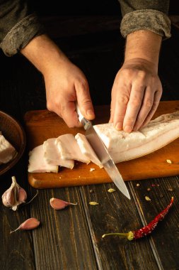 Eller, sarımsak karanfilleri ve parlak kırmızı biberle çevrili ahşap bir kesme tahtasındaki taze domuz etini ustalıkla dilimliyor. Sakin bir mutfak atmosferi aşçılık sanatını geliştirir..