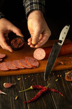 Ellerin yemekten önce dilimlenmiş salam sosisine ustaca aromatik baharatlar serpiyor. Aşçılık sanatı konsepti.