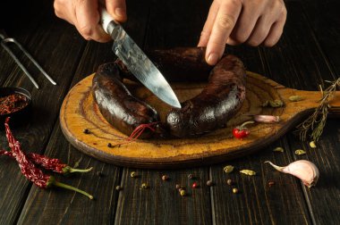 The chef prepares a national dish with spices and pepper at home. Blood sausage is cut by the cook hands with a knife on a kitchen cutting board. clipart