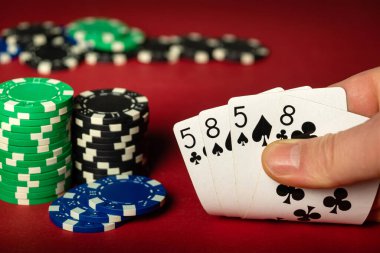 Oyuncu kırmızı poker masasında iki çift kazanan kombinasyonla iskambil oynar. Kumarhanedeki kartlarla el ve çip oynamaya yakın plan..