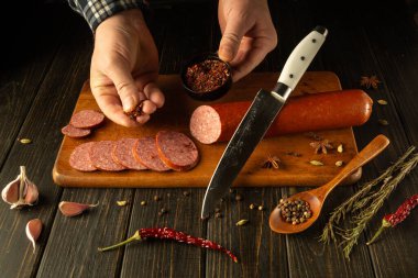 Eller ustalıkla dilimlenmiş sosisin üzerine aromatik baharatlar serpiyor. Yemek pişirme becerisi ya da akşam yemeği için et yemeği hazırlama kavramı.