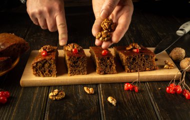 Hands skillfully arrange a delightful dessert on a rustic wooden board, garnishing with walnuts and viburnum. The warm, inviting atmosphere creates an enticing culinary experience. clipart