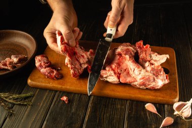 Yetenekli eller, taze sarımsak ve bitkilerle çevrili ahşap bir tahtanın üzerinde ustalıkla çiğ et kesiyor. Mutfak macerasına dair samimi ipuçları ortaya çıkmaya hazır..