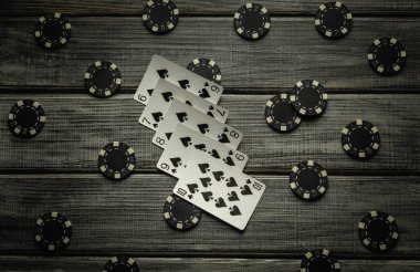 Heyecan verici bir poker oyunu, düz bir floş kombinasyonu ve çeşitli poker fişleri içeren, kırsal ahşap bir masanın üzerinde sergileniyor, oyuncular için gergin bir atmosfer yaratıyor..