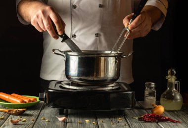 Tecrübeli bir aşçı fırının içindekileri karıştırırken bıçak ve çatal ustalıkla manevra yapar. Yakınlarda soğan ve sarımsak gibi taze malzemeler bulunmakta ve pişirme alanına renk katmaktadır..