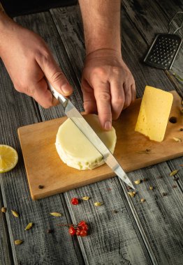 Yetenekli eller tahtadan bir yuvarlak peyniri taze limon ve baharatlarla dilimliyor. Sıcak mutfak sıcak bir atmosfer yayar, mutfak yaratımı için mükemmeldir..